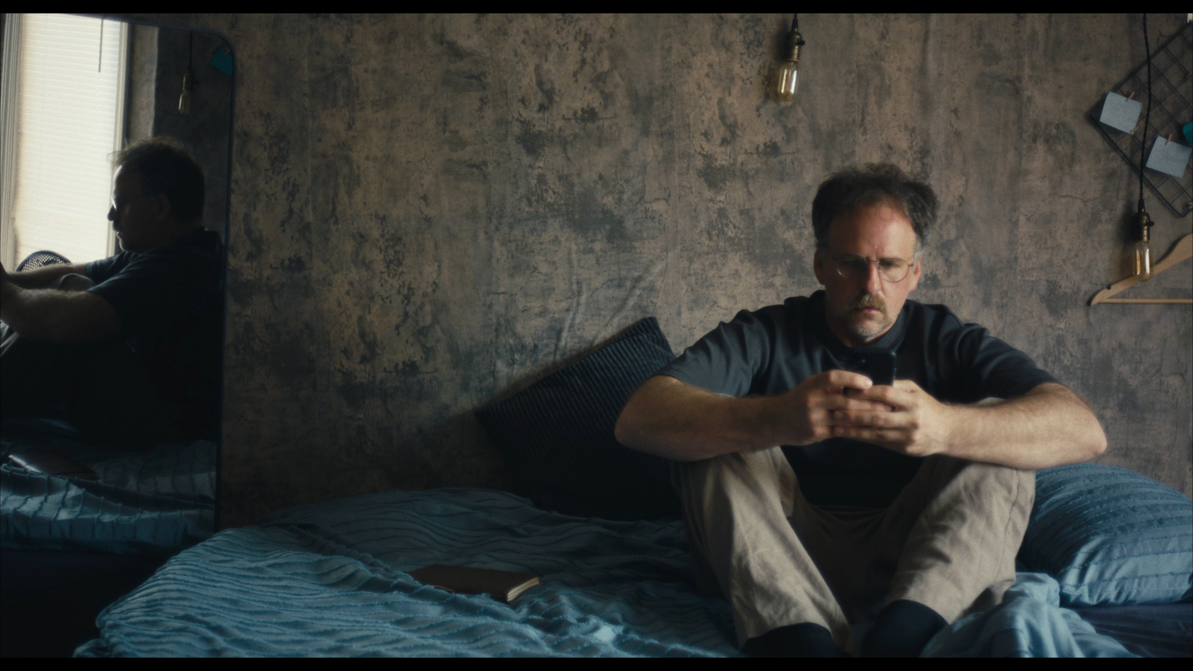 A man seated on a bed looking at his phone