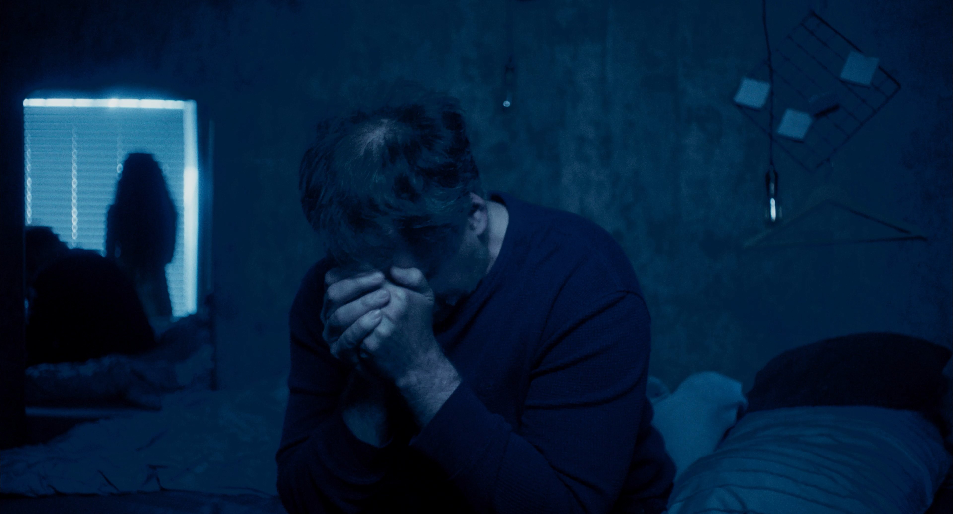 A man sitting in a dark blue bedroom
