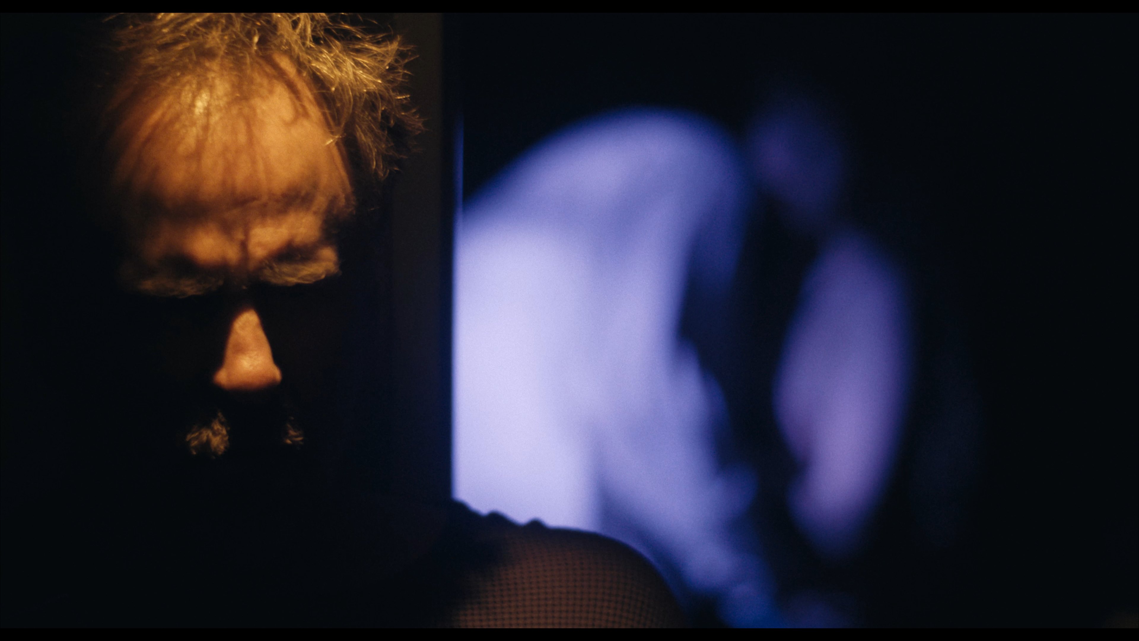 A man's face lit with amber and blue light