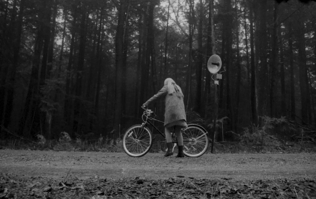 A figure stands with a bicycle beside a loudspeaker